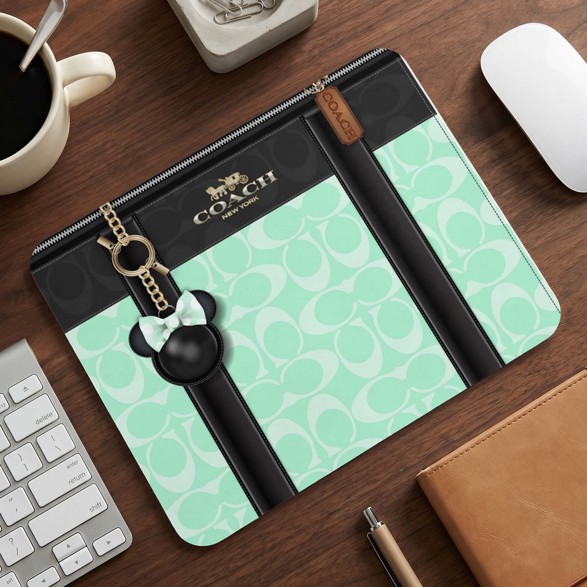Coach laptop sleeve with mint green signature pattern and Mickey Mouse charm.