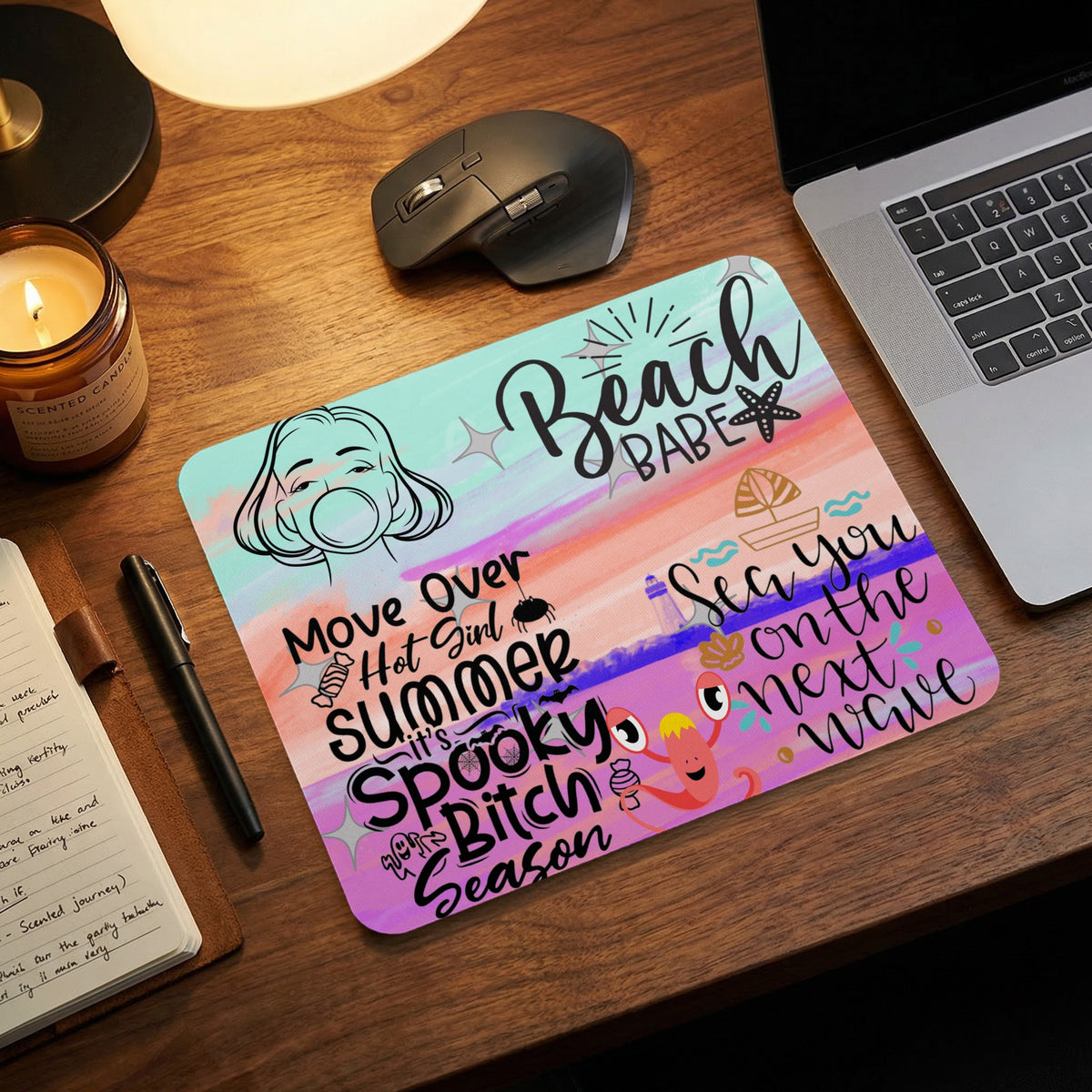 A colorful mousepad on a wooden desk features pastel brushstrokes and beach and Halloween text.
