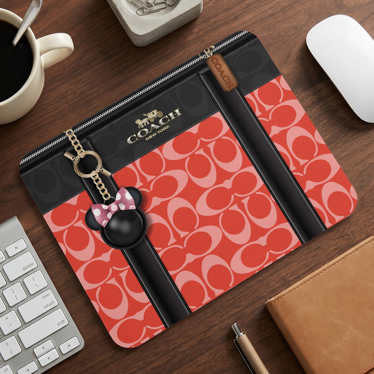 Coach laptop sleeve with signature print and Minnie Mouse charm on desk.