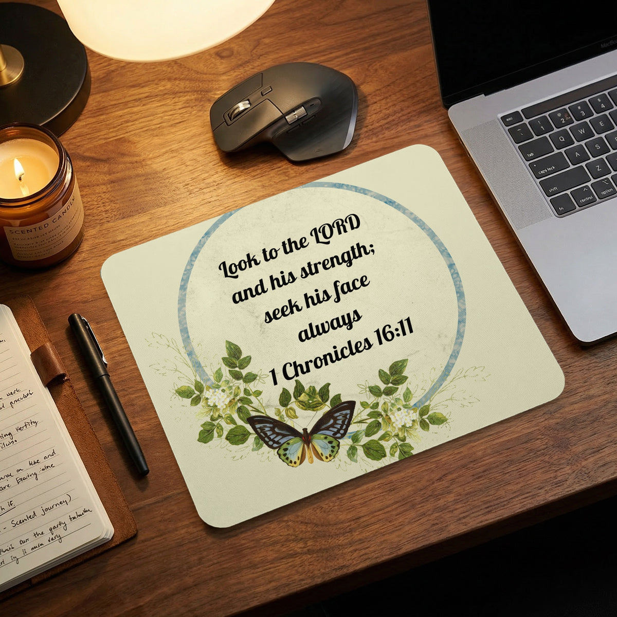 A light-colored mousepad featuring a Bible verse, green foliage, and a butterfly on a wooden desk.
