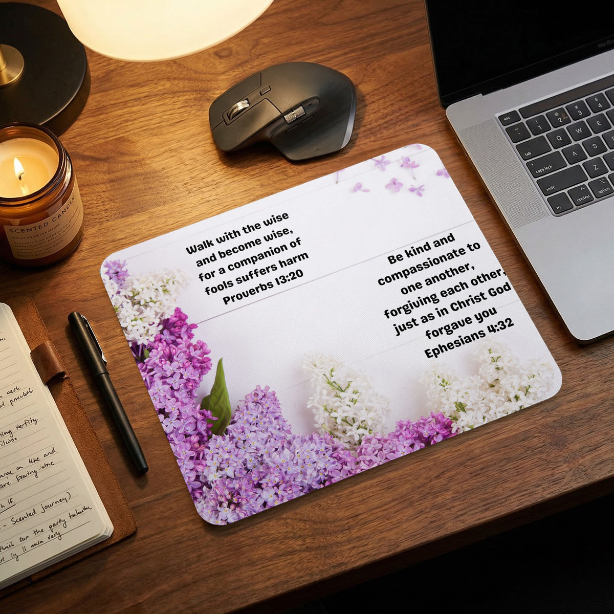 A mouse pad featuring white and purple lilac flowers with Bible verses on a wooden desk.
