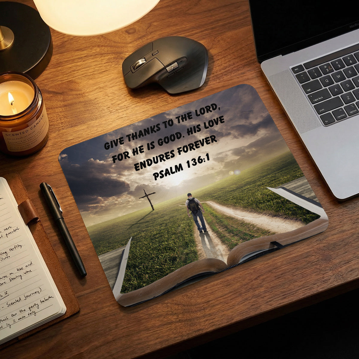 A rectangular mousepad featuring an open book graphic with a landscape, cross, and Psalm 136:1 text.