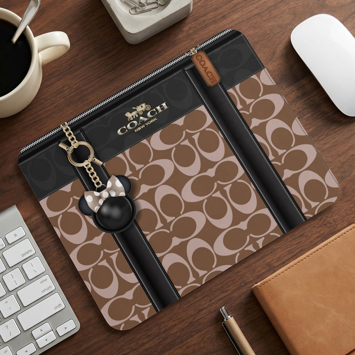 Coach monogram laptop sleeve with Minnie Mouse keychain on a wooden desk.