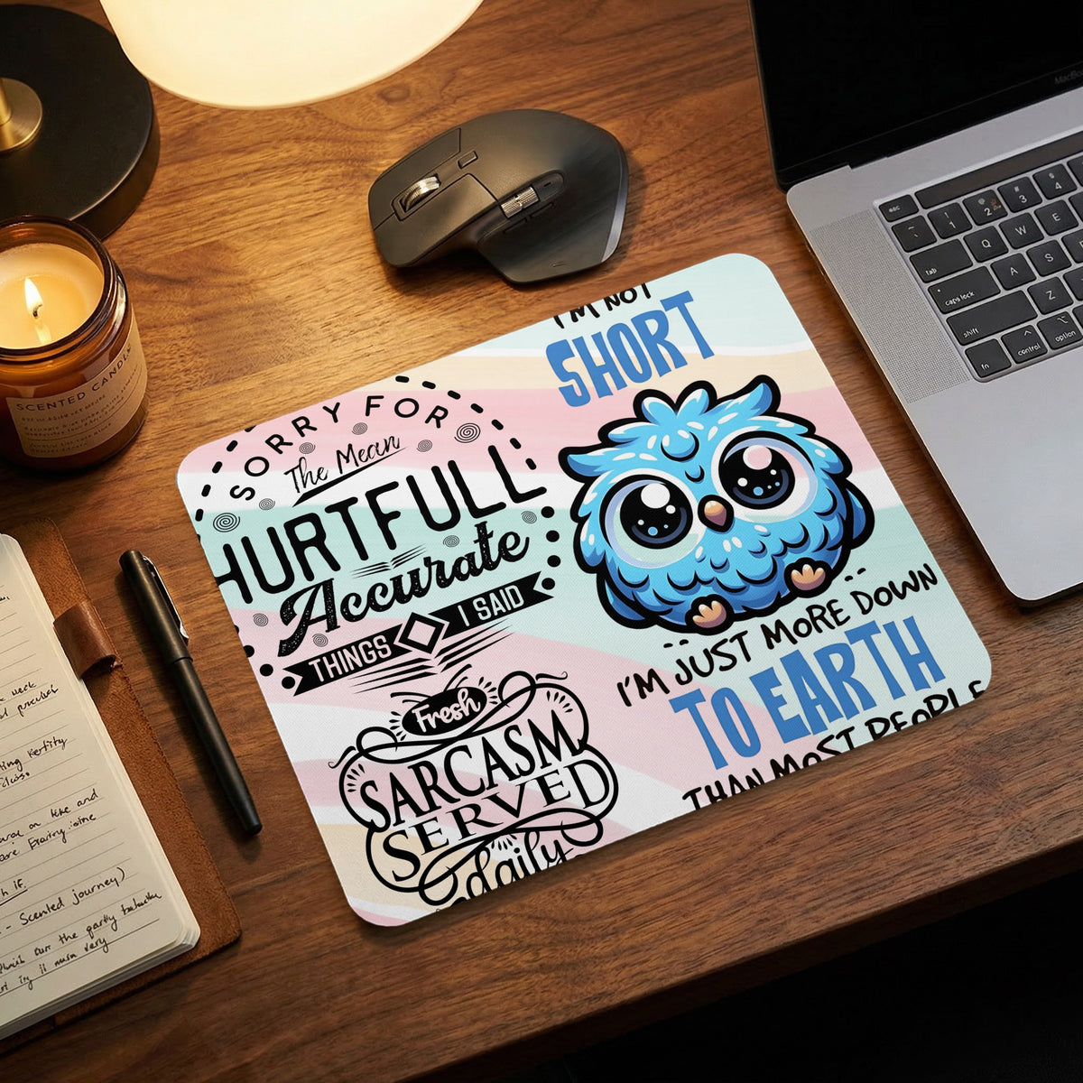 A mouse pad on a wooden desk with humorous text and a cute blue owl illustration.