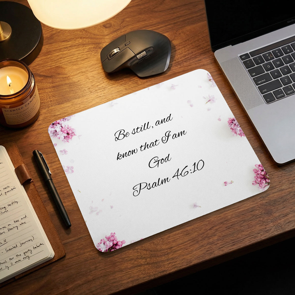 A white mousepad featuring pink floral accents and the Bible verse Psalm 46:10 on a wooden desk.