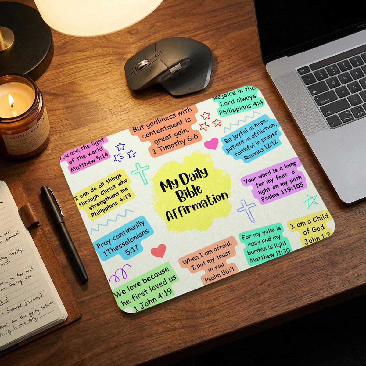 A desk mat featuring daily Bible affirmations, surrounded by a laptop, candle, mouse, and notebook.