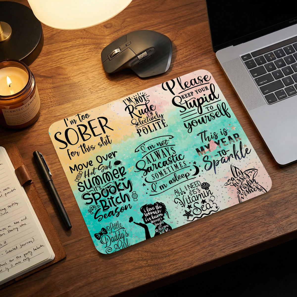 Colorful desk mat with sarcastic quotes, placed on a wooden desk near a laptop, mouse, and candle.