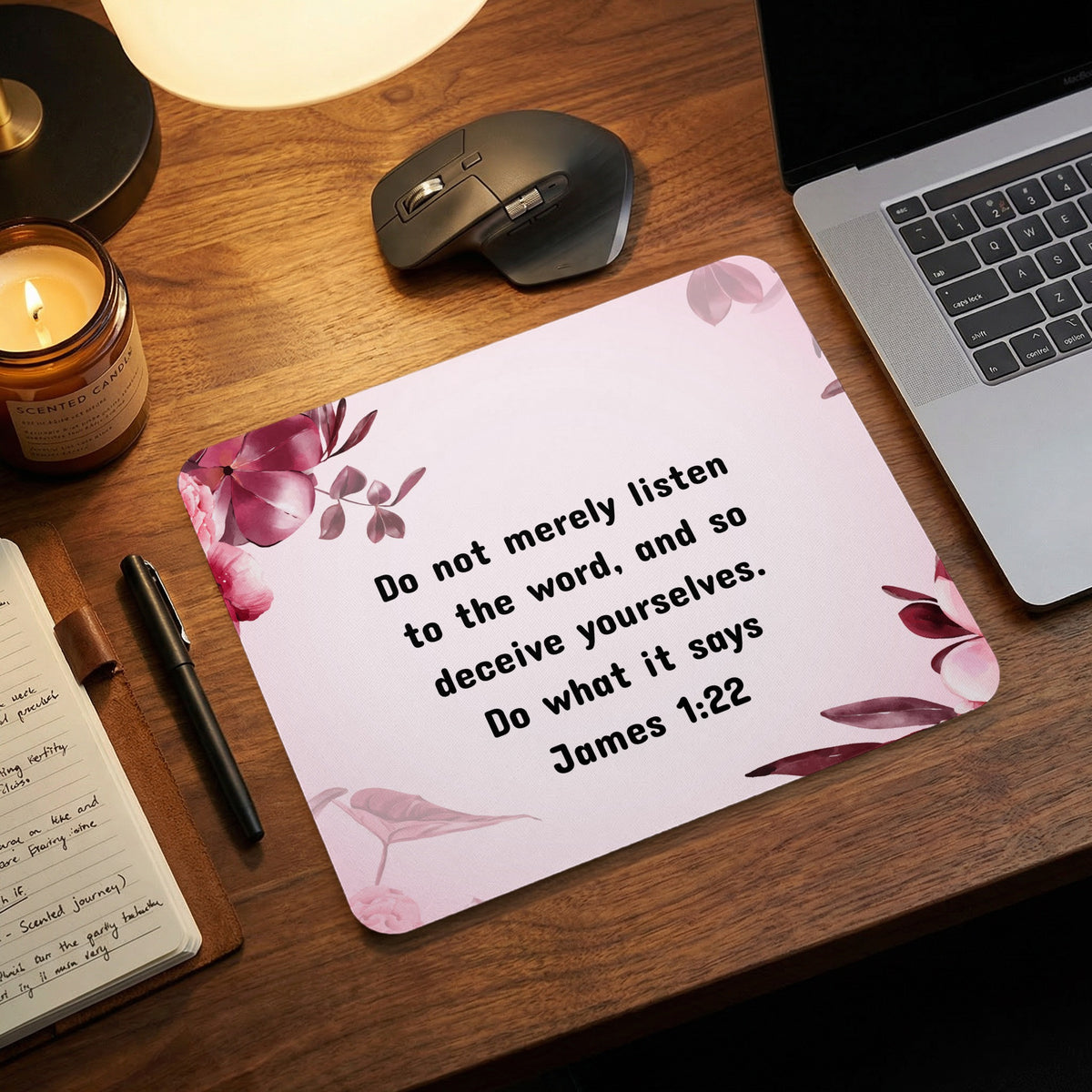 A pink mouse pad featuring the James 1:22 Bible verse surrounded by floral artwork on a wooden desk.