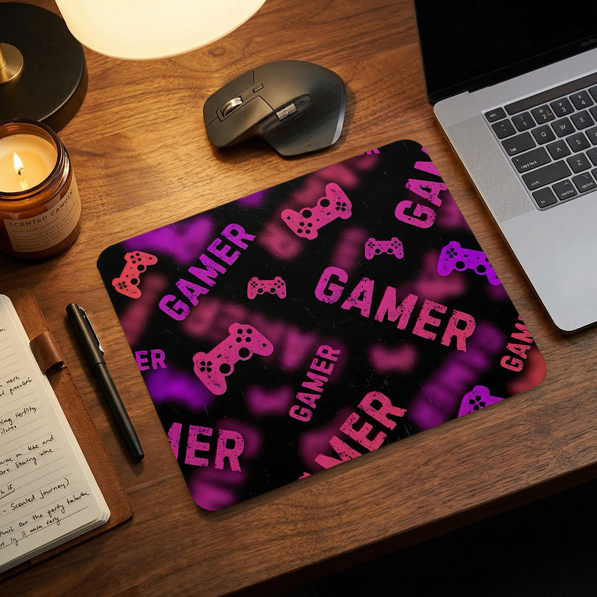 A black and pink gaming mousepad on a wooden desk with a laptop, mouse, and notebook.