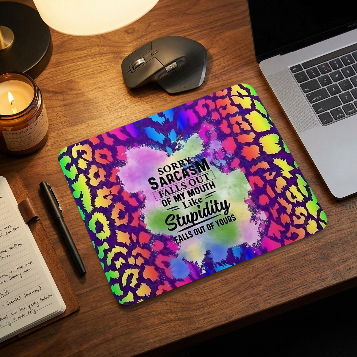 A colorful rainbow leopard print mouse pad with sarcastic text rests on a wooden desk.