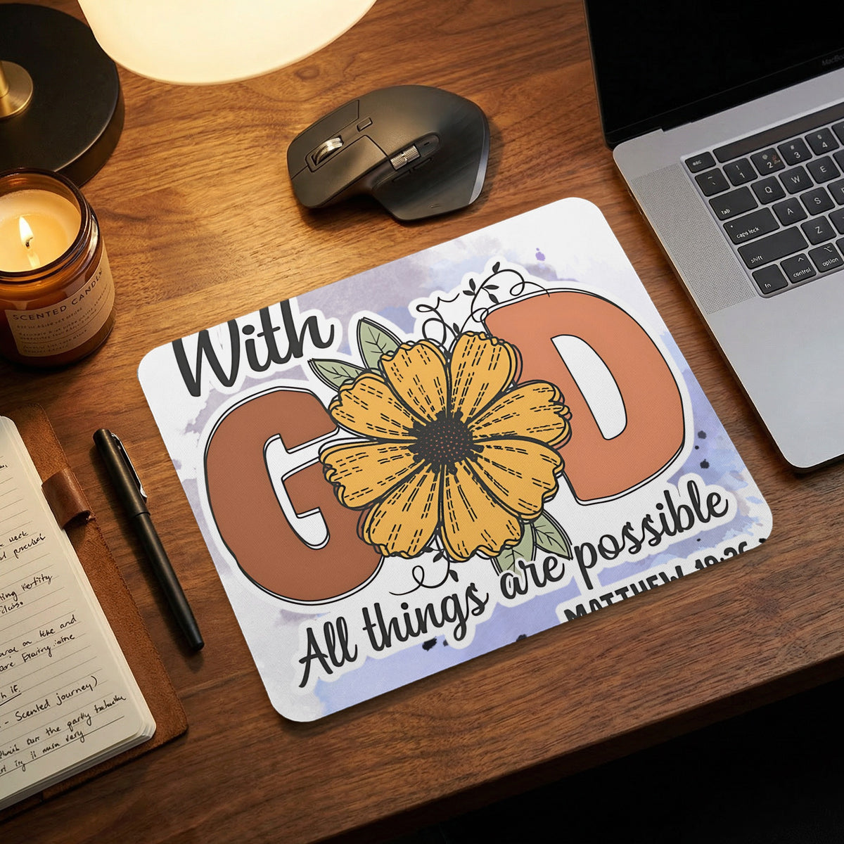 A mouse pad with a floral design and the text With God All things are possible sits on a wooden desk.