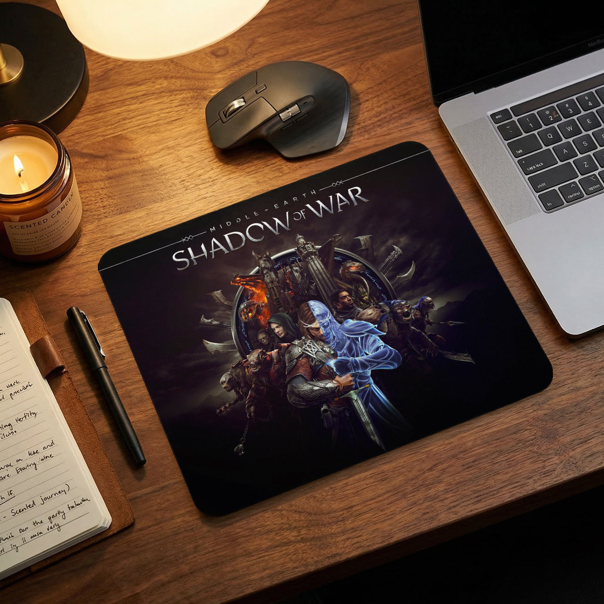 A black gaming mouse pad featuring the Shadow of War video game logo and characters, displayed on a wooden desk.