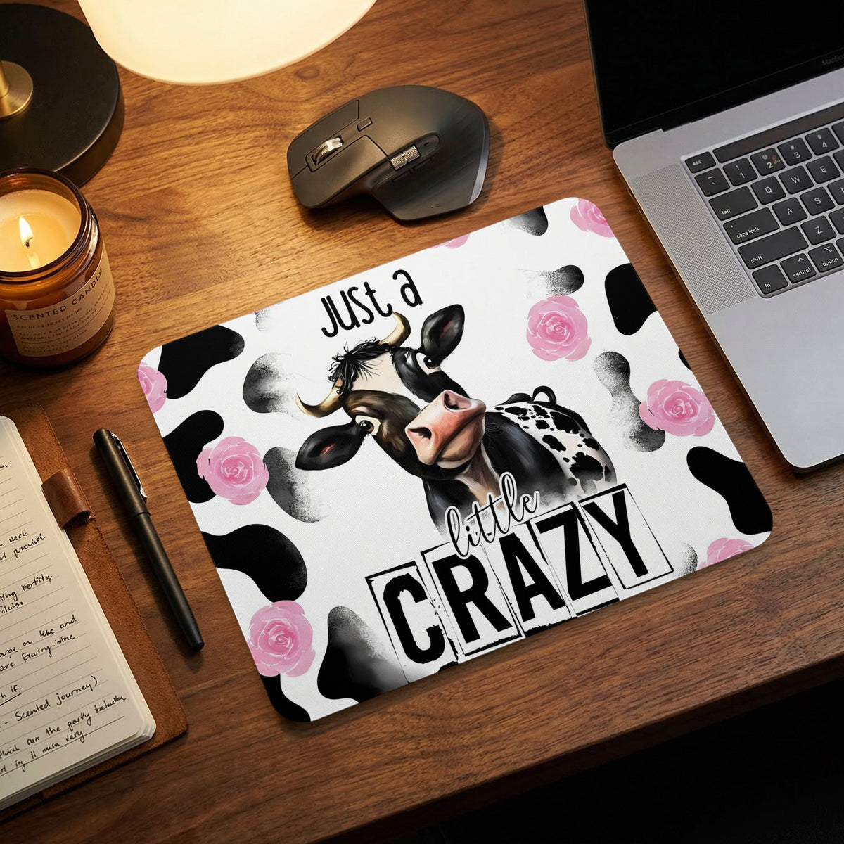 Cow print mousepad with pink roses and text that reads Just a little CRAZY on wooden desk.