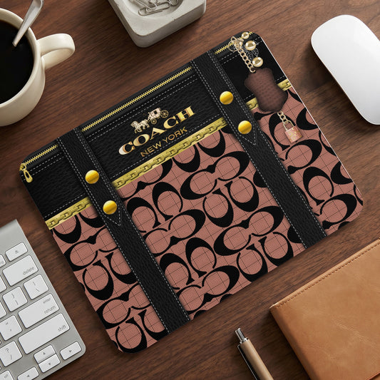 Coach print mousepad with gold hardware and zipper details on wood surface.