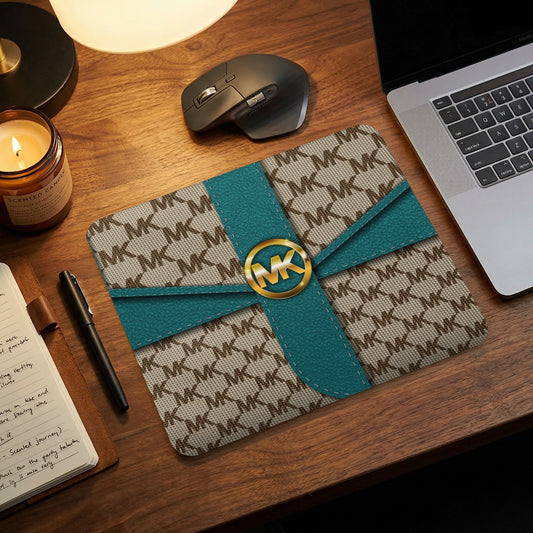 Michael Kors MK logo mousepad with teal ribbon detail and gold emblem.