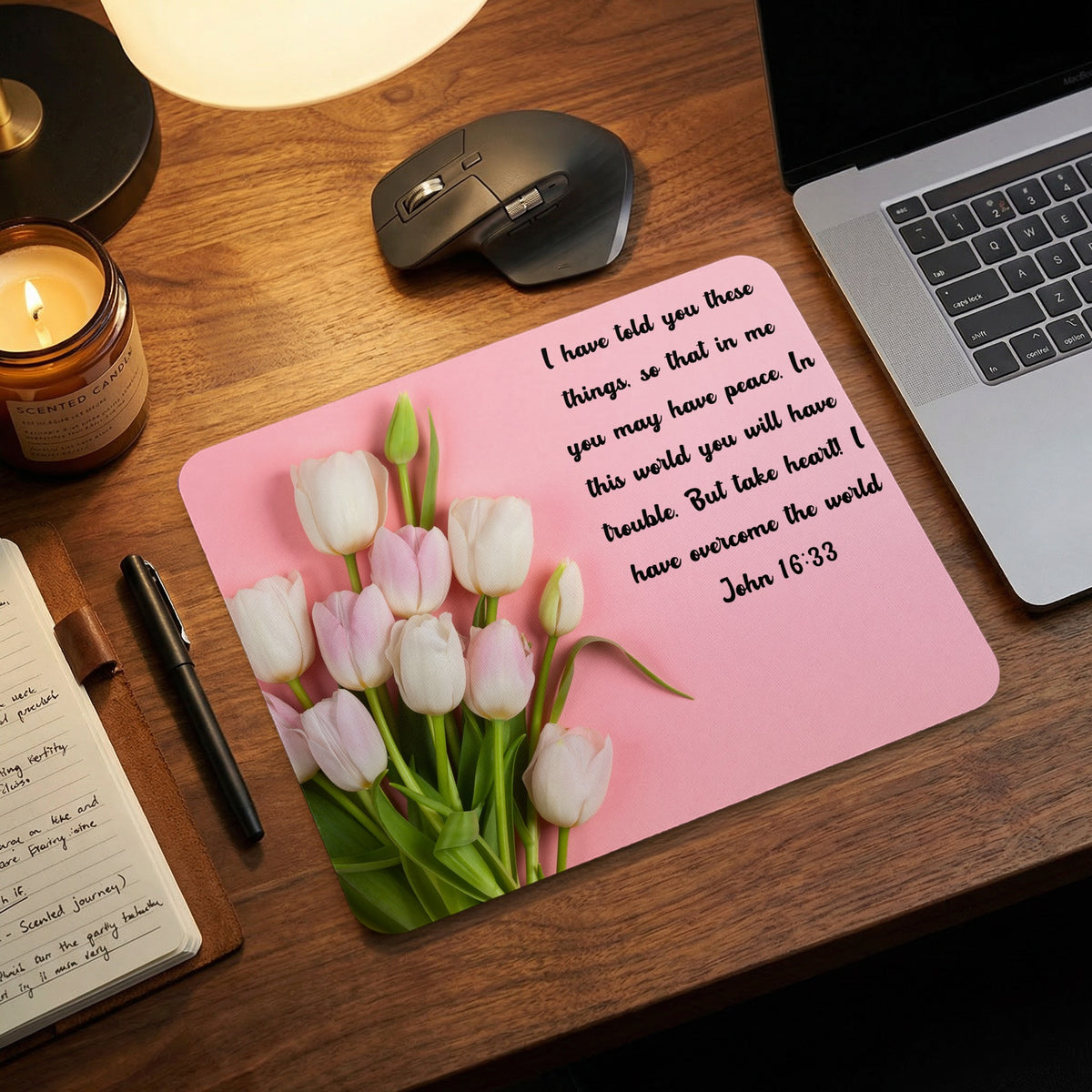 Pink mouse pad on a wooden desk featuring white tulips and Bible verse John 16:33.