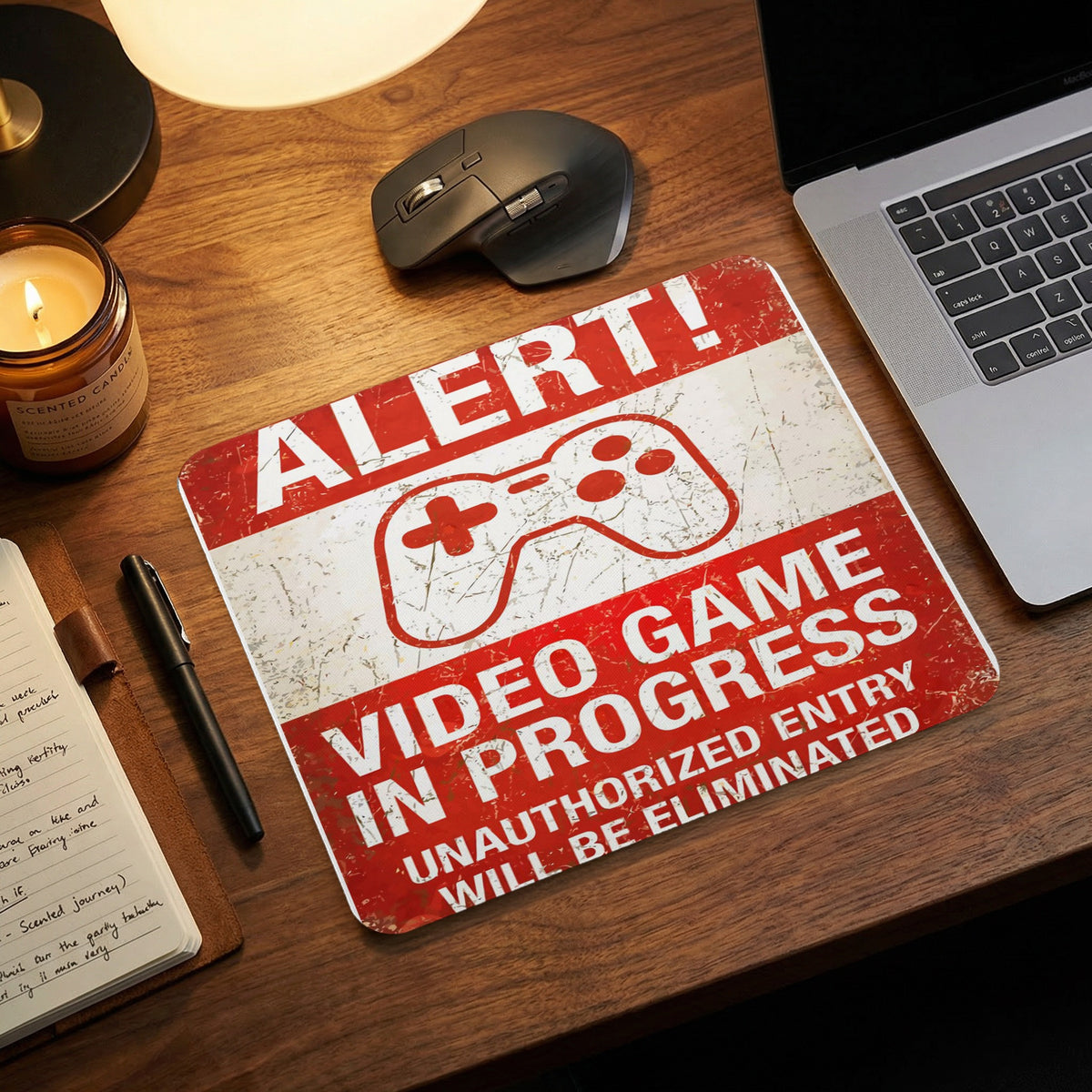 A red and white distressed mousepad with text reading ALERT! VIDEO GAME IN PROGRESS, UNAUTHORIZED ENTRY WILL BE ELIMINATED, placed on a wooden desk.