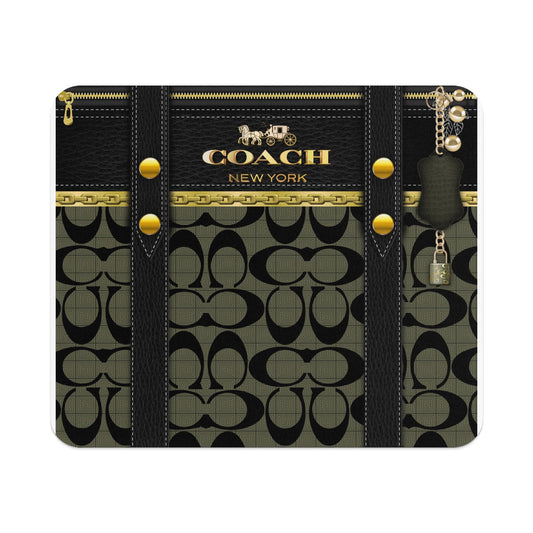 A rectangular mousepad featuring a Coach New York monogram pattern with black leather straps and gold hardware.
