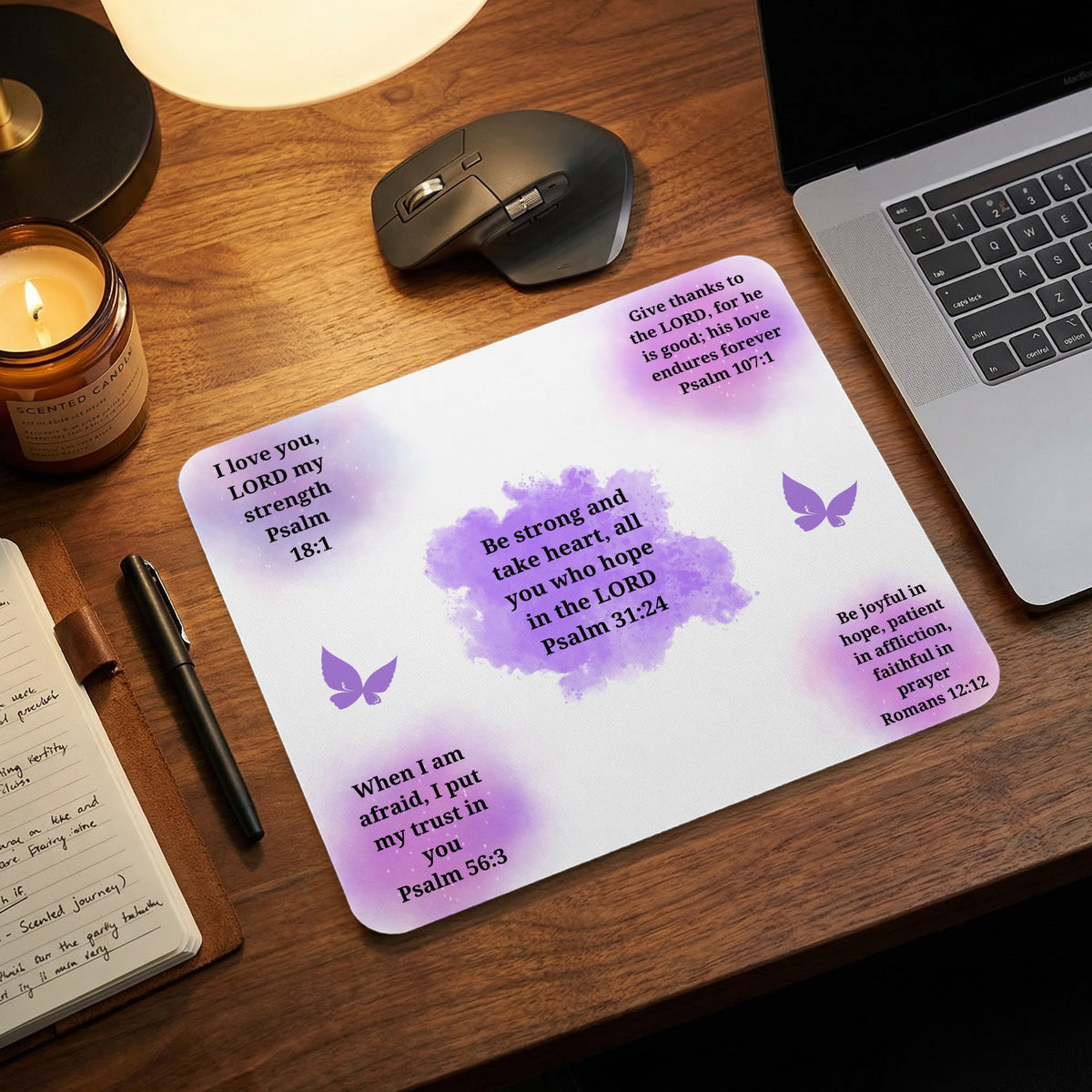 A white mouse pad with purple watercolor splashes, motivational Bible verses, and butterflies rests on a wooden desk.