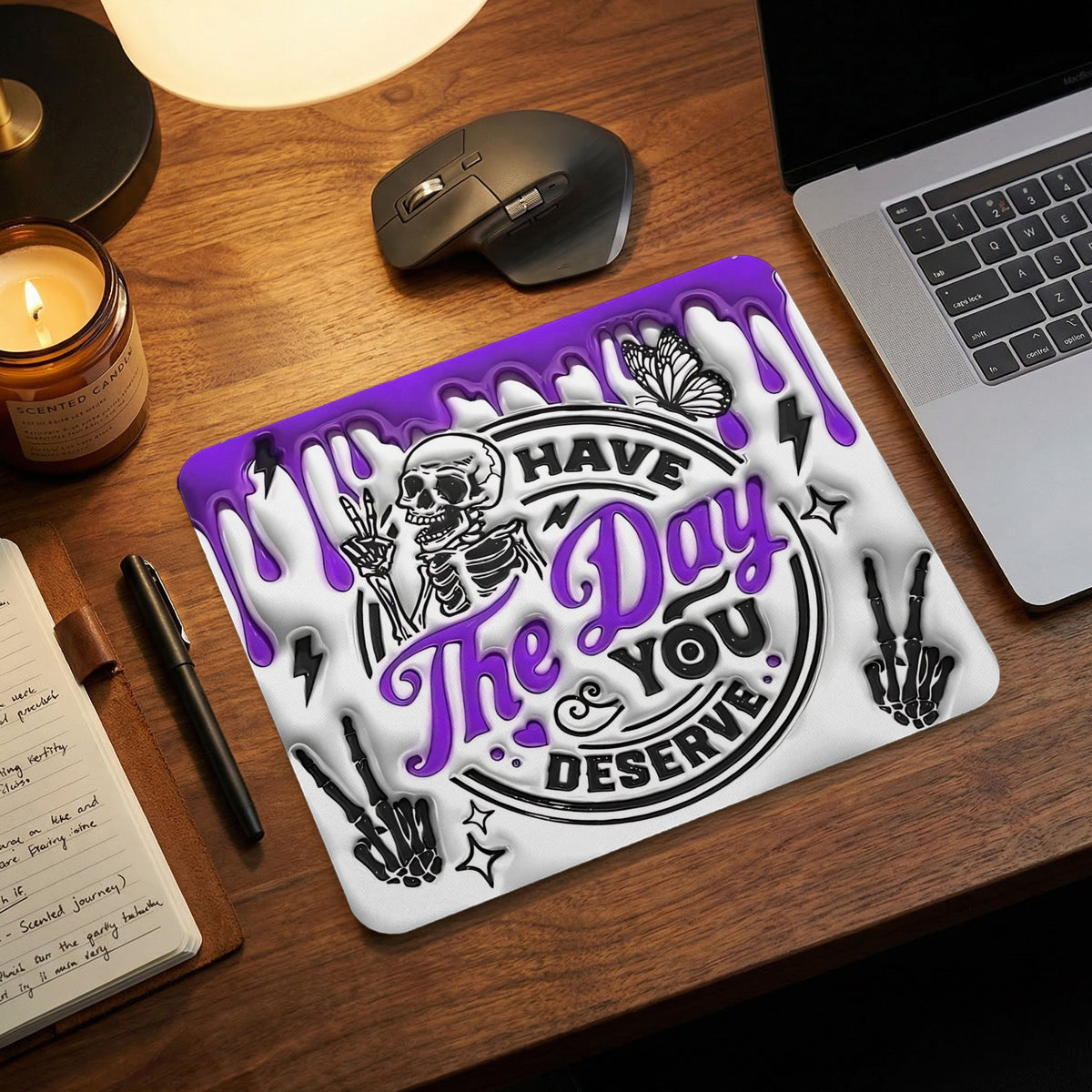 Purple and white mouse pad with a skeleton graphic and the text have the day you deserve on a wooden desk.