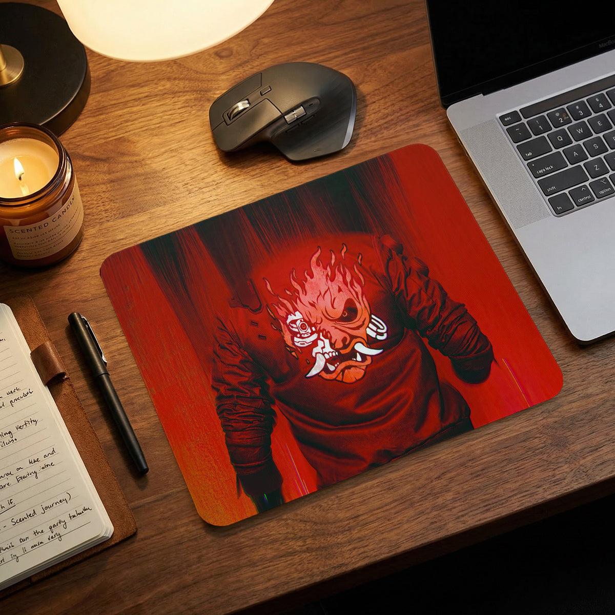 A red mousepad featuring a stylized samurai demon graphic on a wooden desk with a laptop and mouse.