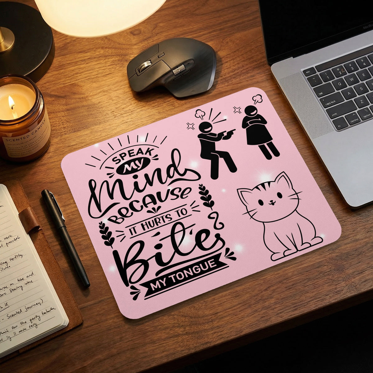 A pink mousepad with black text and illustrations of a cat and angry figures sits on a wooden desk.