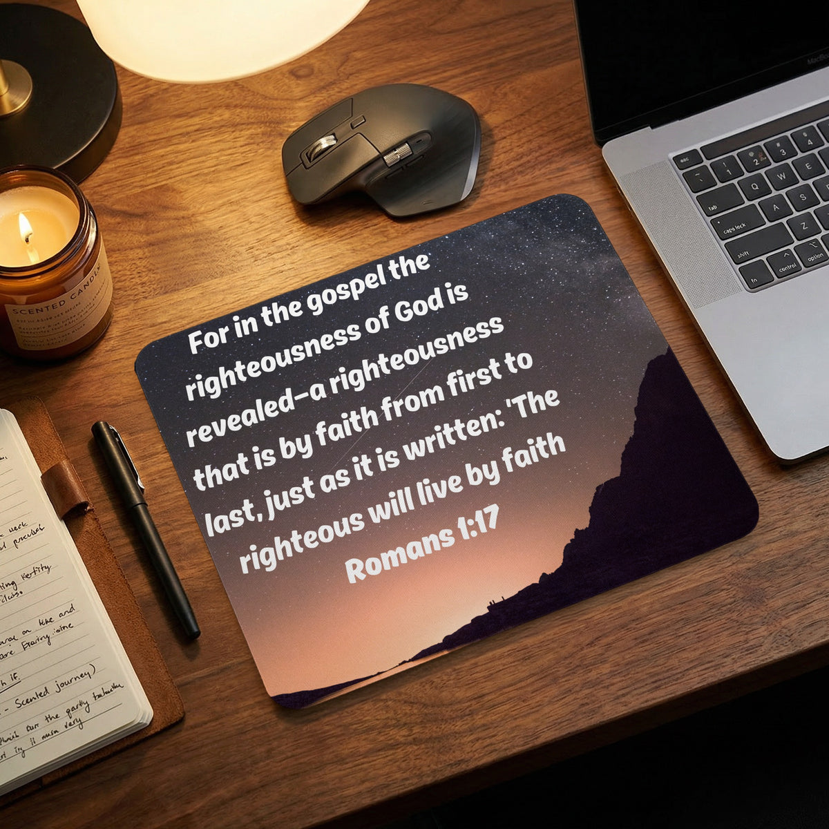 A rectangular mouse pad with the Bible verse Romans 1:17 printed over a mountain sunset background.