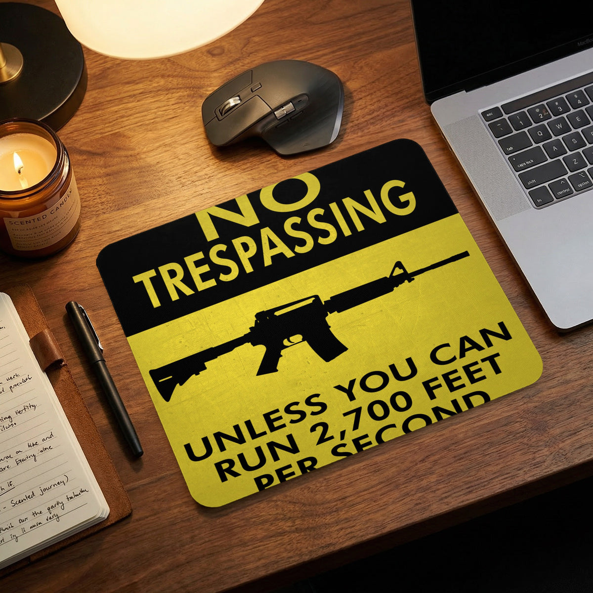 A black and yellow mousepad featuring an assault rifle silhouette and warning text on a wooden desk.