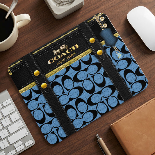 Coach pattern mousepad with gold hardware and charm on wooden desk.