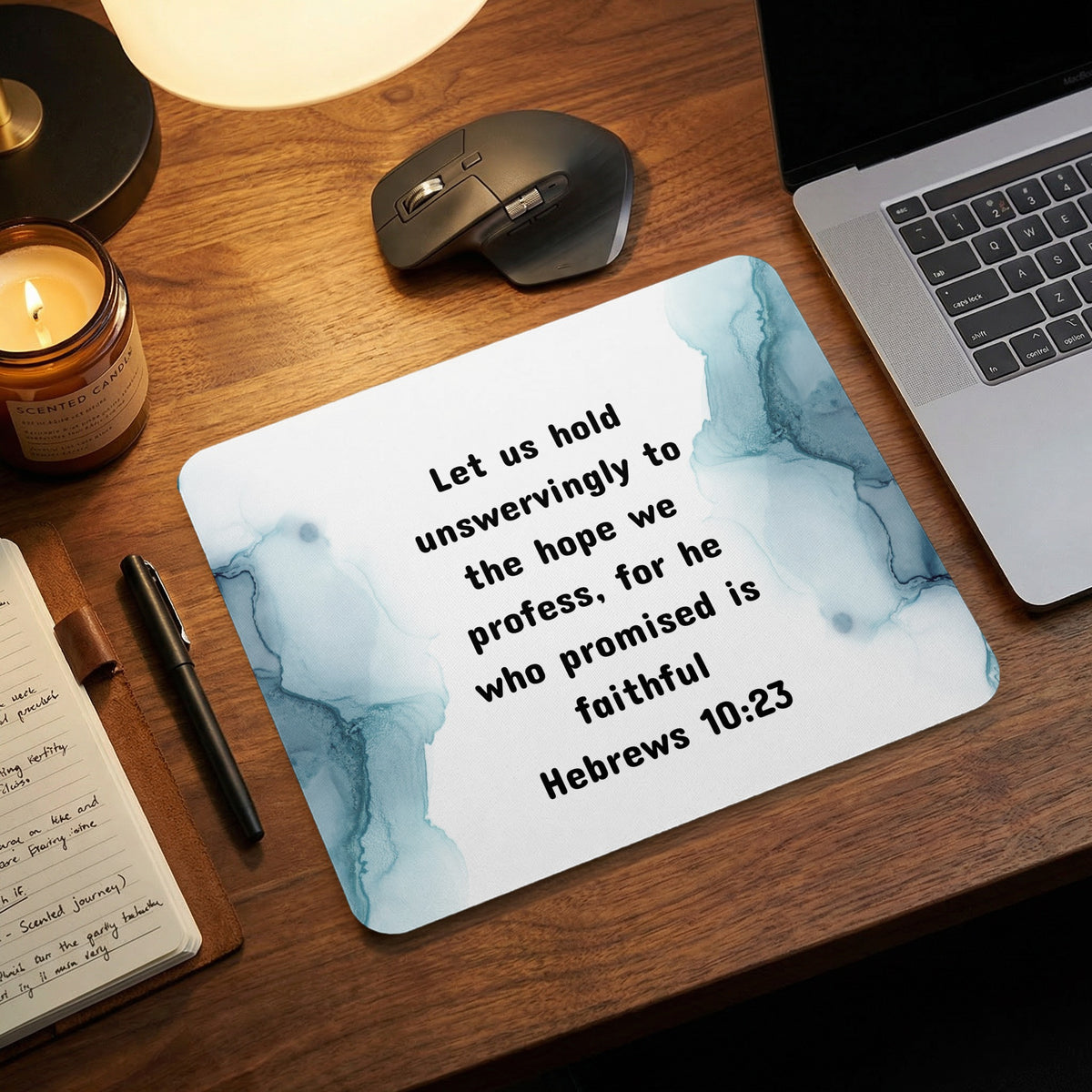 A light blue and white mousepad printed with Hebrews 10:23 sits on a wooden desk.