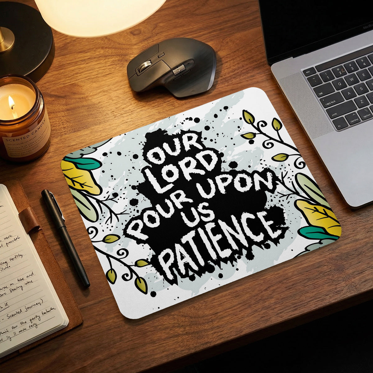 A rectangular mousepad featuring the text Our Lord Pour Upon Us Patience on a wooden desk.