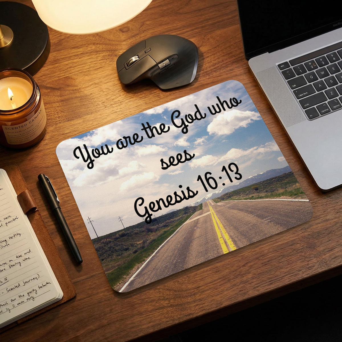 A rectangular mouse pad with a road and sky design and Bible verse text on a wooden desk.