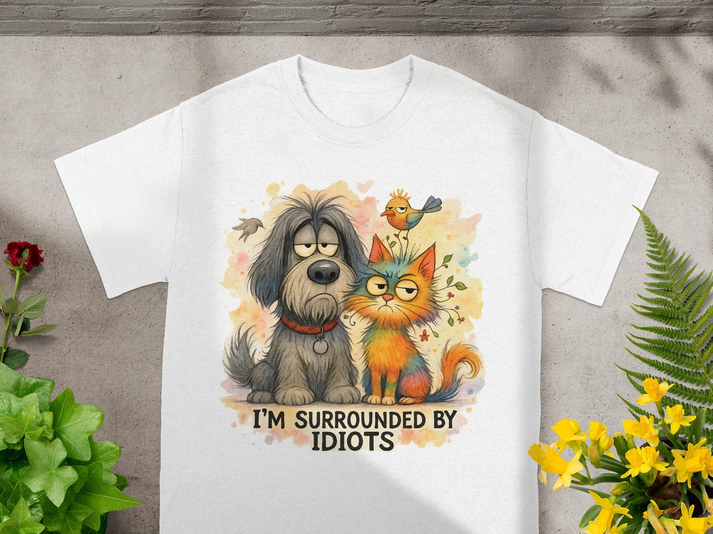 White t-shirt with watercolor illustration of a sad dog and a grumpy cat with the text "I'M SURROUNDED BY IDIOTS".