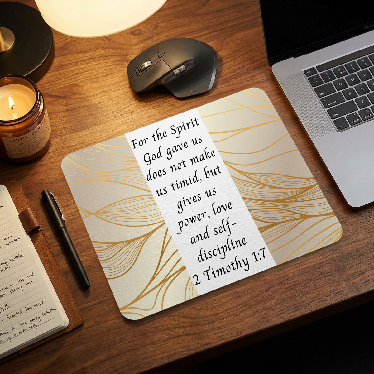 A mouse pad featuring the Bible verse 2 Timothy 1:7 rests on a wooden desk with a laptop and candle.
