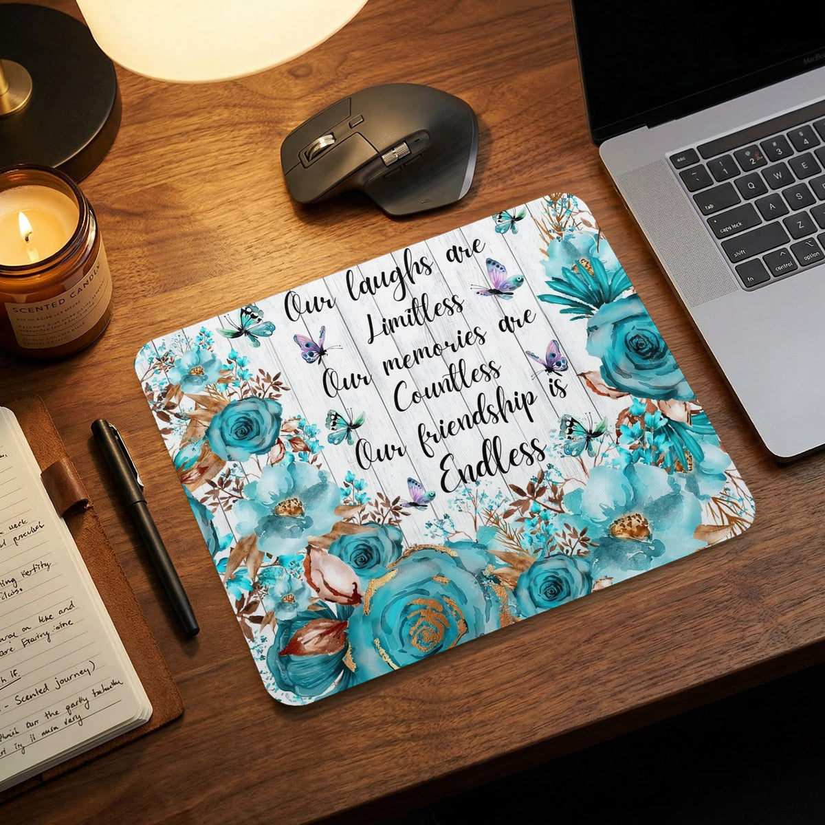 Teal floral mousepad with a friendship quote on a wooden desk with laptop, mouse, and candle.