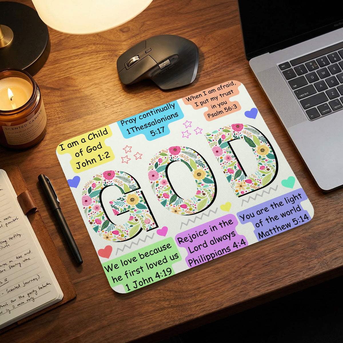 Christian mouse pad featuring floral letters spelling GOD and Bible verses, on a wooden desk.