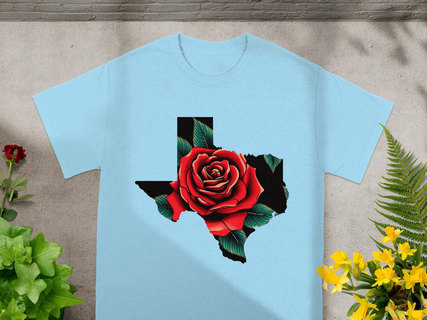 Light blue t-shirt with Texas outline filled by a red rose with green leaves.