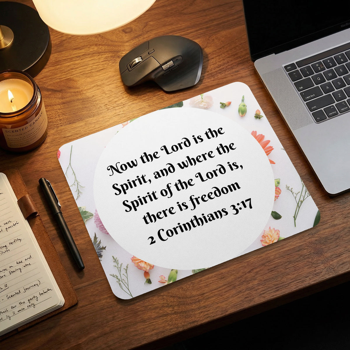 A rectangular mousepad featuring a floral border and Bible verse is displayed on a wooden desk.