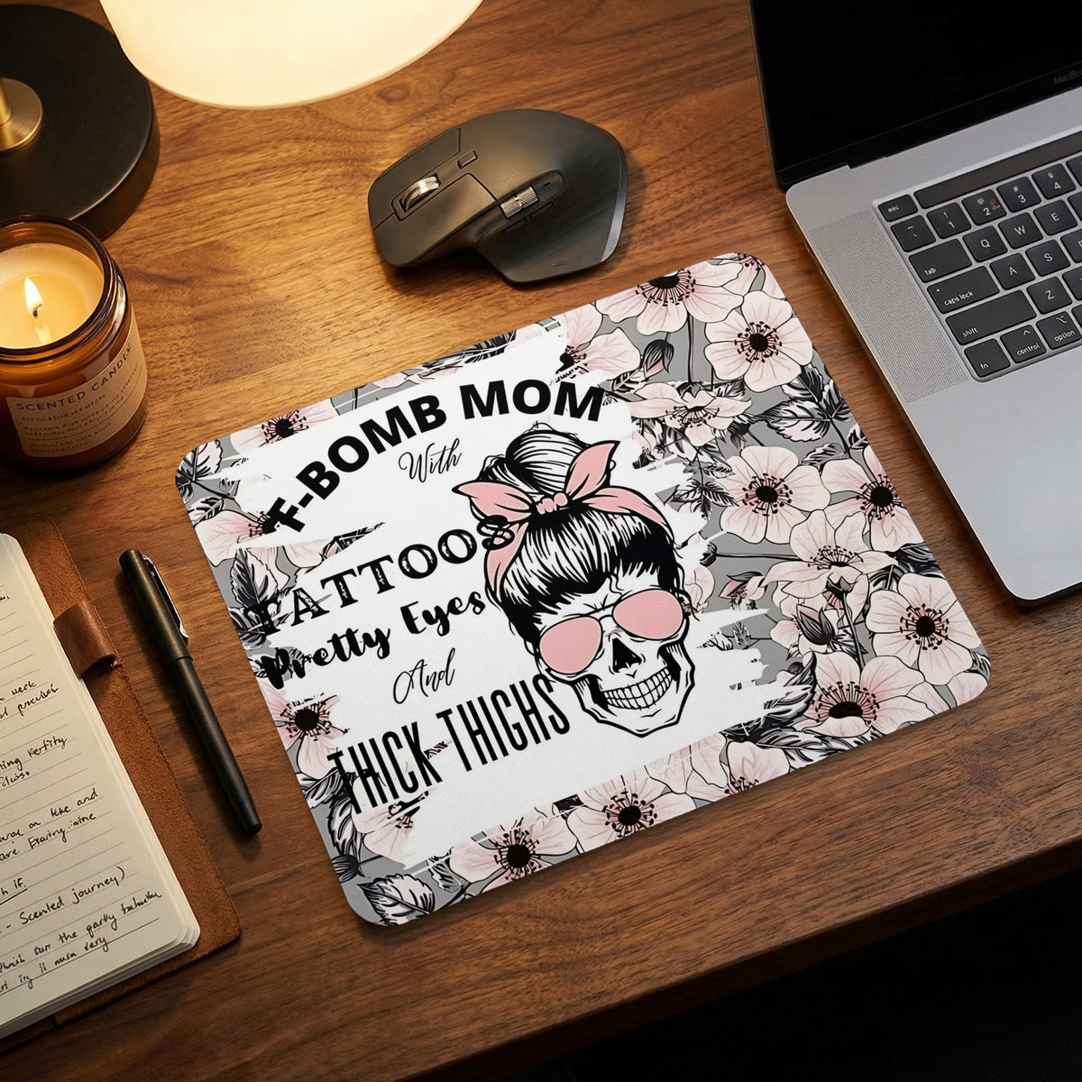 Floral-patterned mouse pad with a skull graphic and text on a wooden desk next to a laptop.