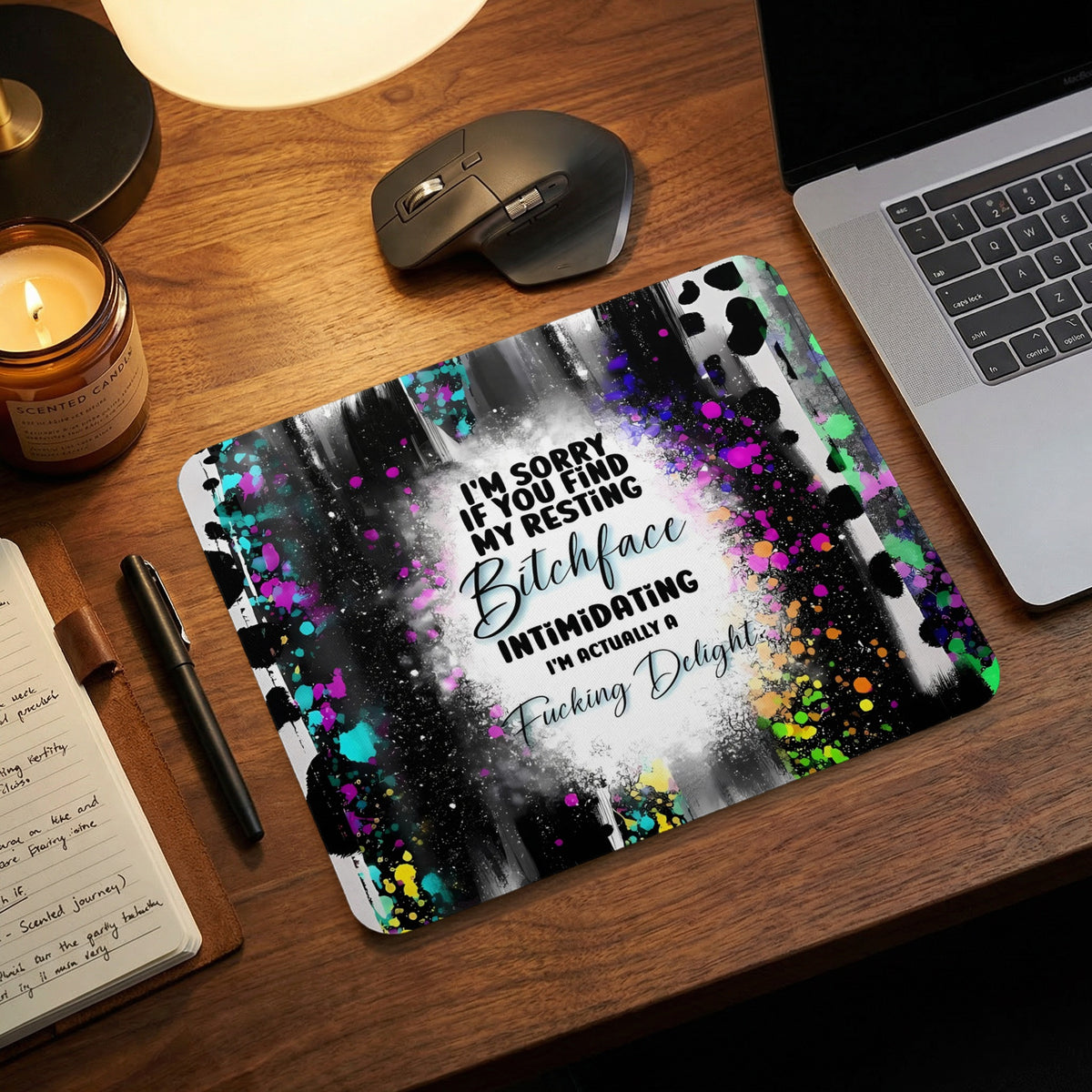 A colorful, abstract mousepad with text reading “I'm sorry if you find my resting bitchface intimidating, I'm actually a fucking delight,” sitting on a wooden desk.