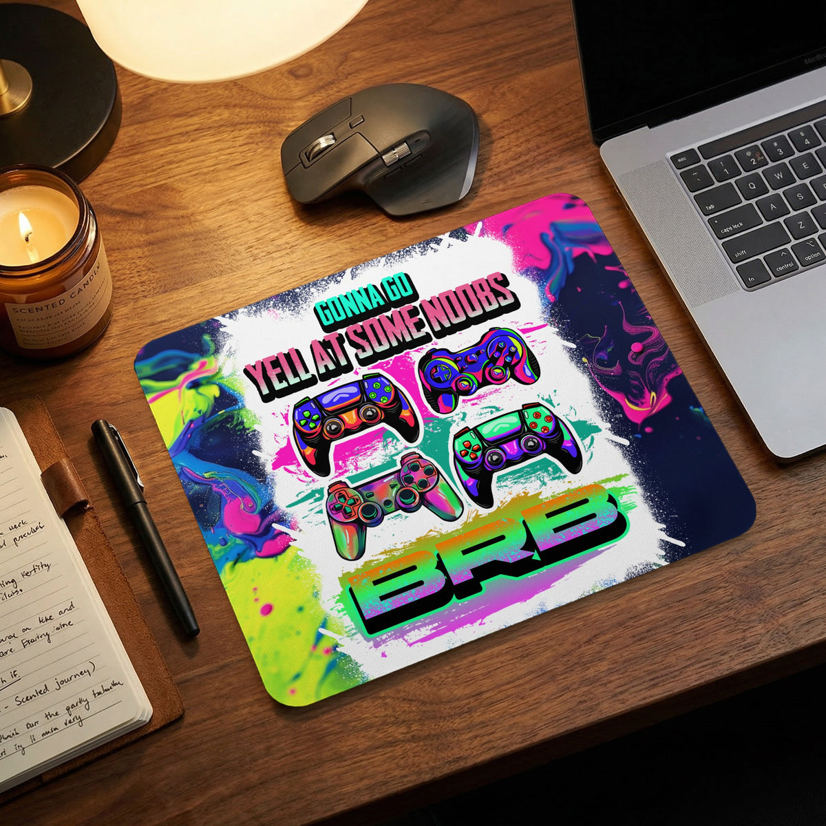 A colorful gaming mouse pad featuring controllers and text reading GONNA GO YELL AT SOME NOOBS BRB on a wooden desk.