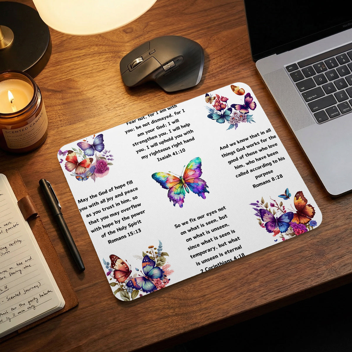 A white mousepad featuring colorful butterflies and Christian Bible verses rests on a wooden desk.
