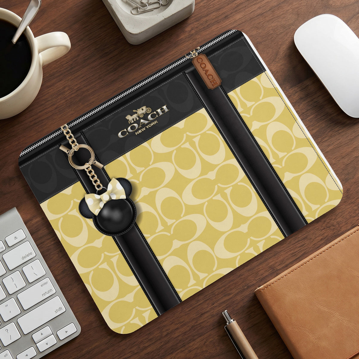 Coach laptop sleeve with yellow monogram pattern and Minnie Mouse charm.
