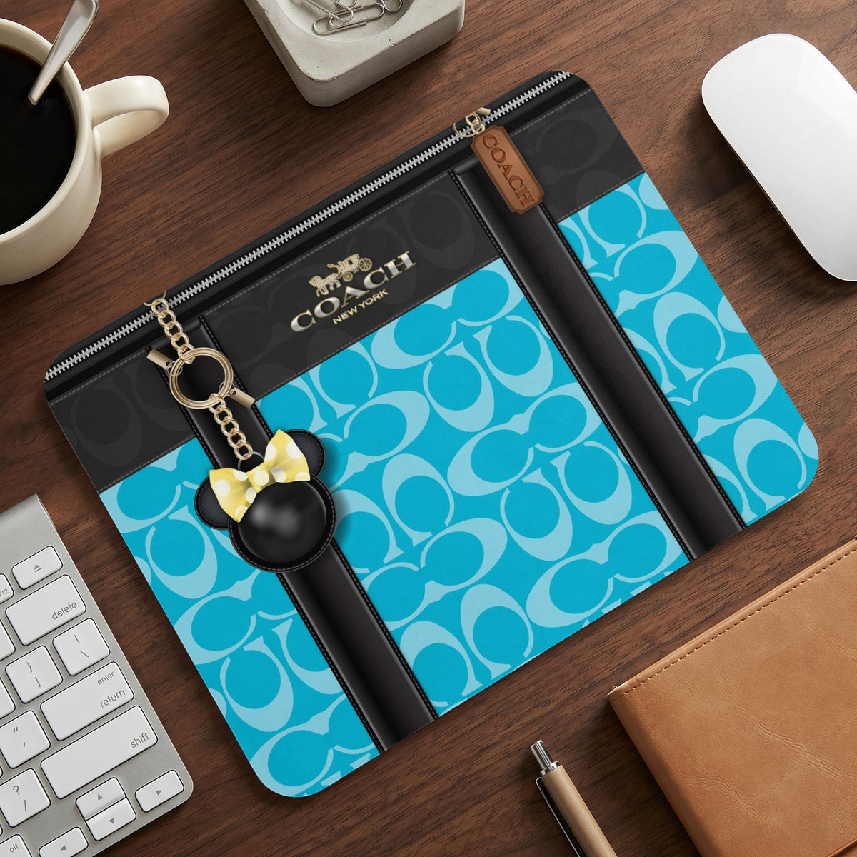 Coach print sleeve with Mickey Mouse charm on a wooden desk.