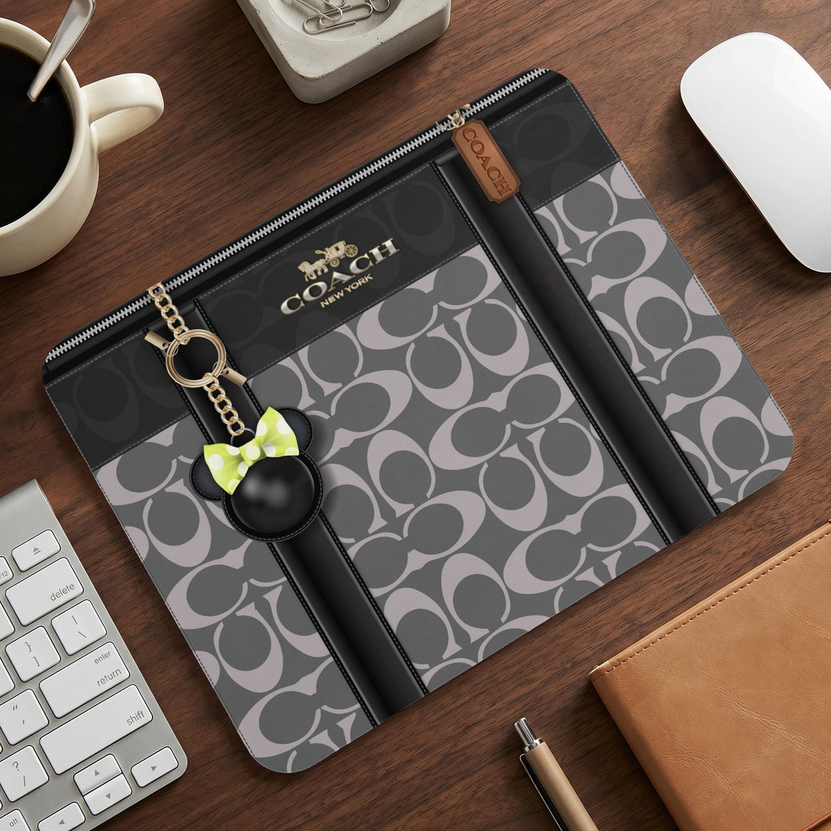 Coach patterned portfolio with a Mickey Mouse charm on a wooden desk.