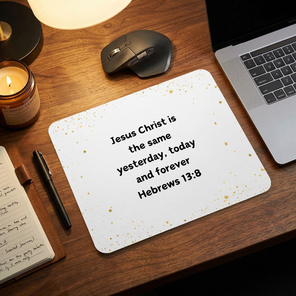 A white mousepad featuring the Bible verse Hebrews 13:8 in black text, surrounded by gold star confetti on a wooden desk.