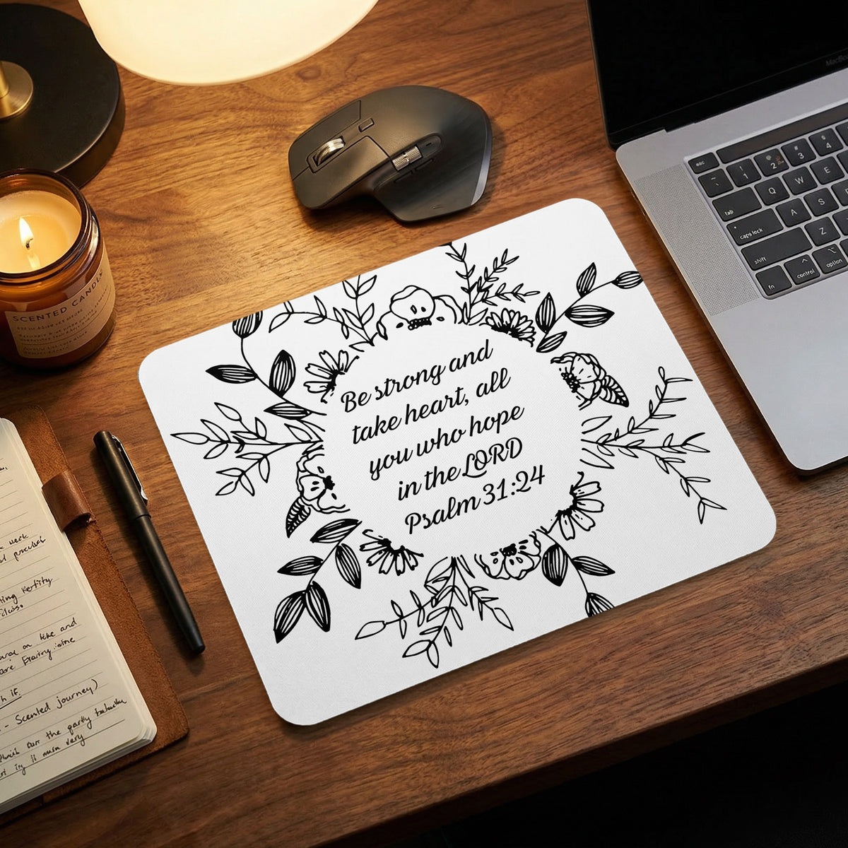 White mousepad featuring black floral border and Psalm 31:24 text rests on wooden desk.