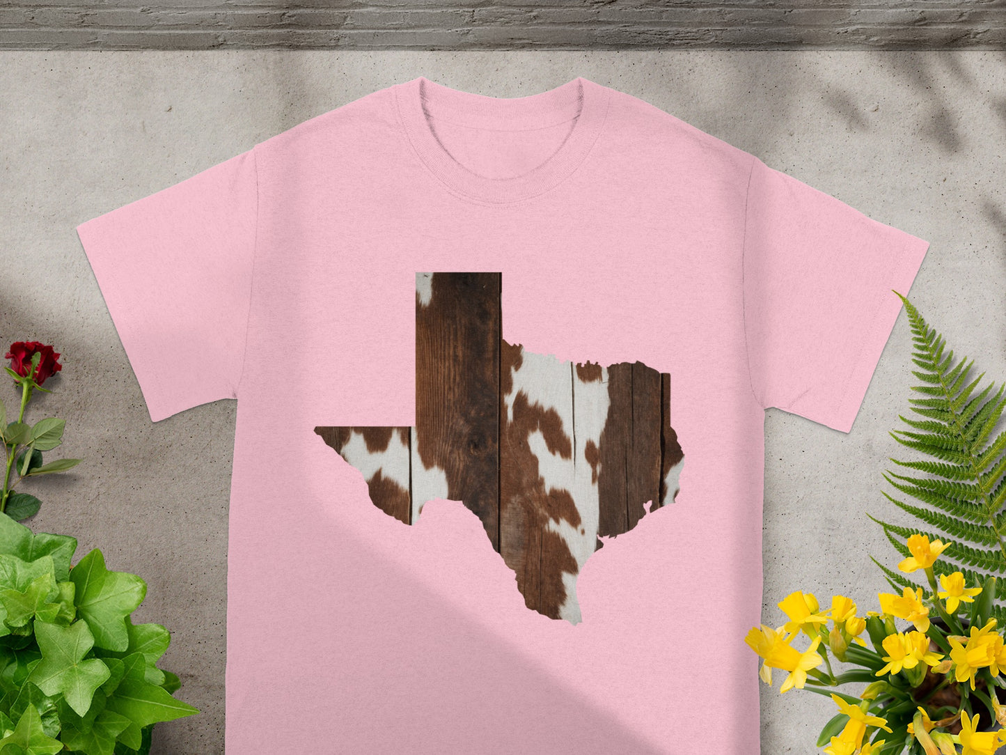 Pink t-shirt with a Texas outline featuring rustic wood and cowhide textures.