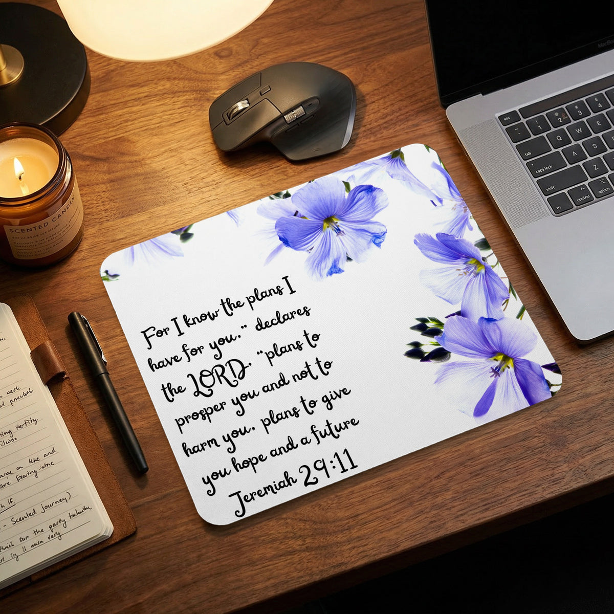 A white mousepad decorated with blue flowers and the Bible verse Jeremiah 29:11 lies on a wooden desk.