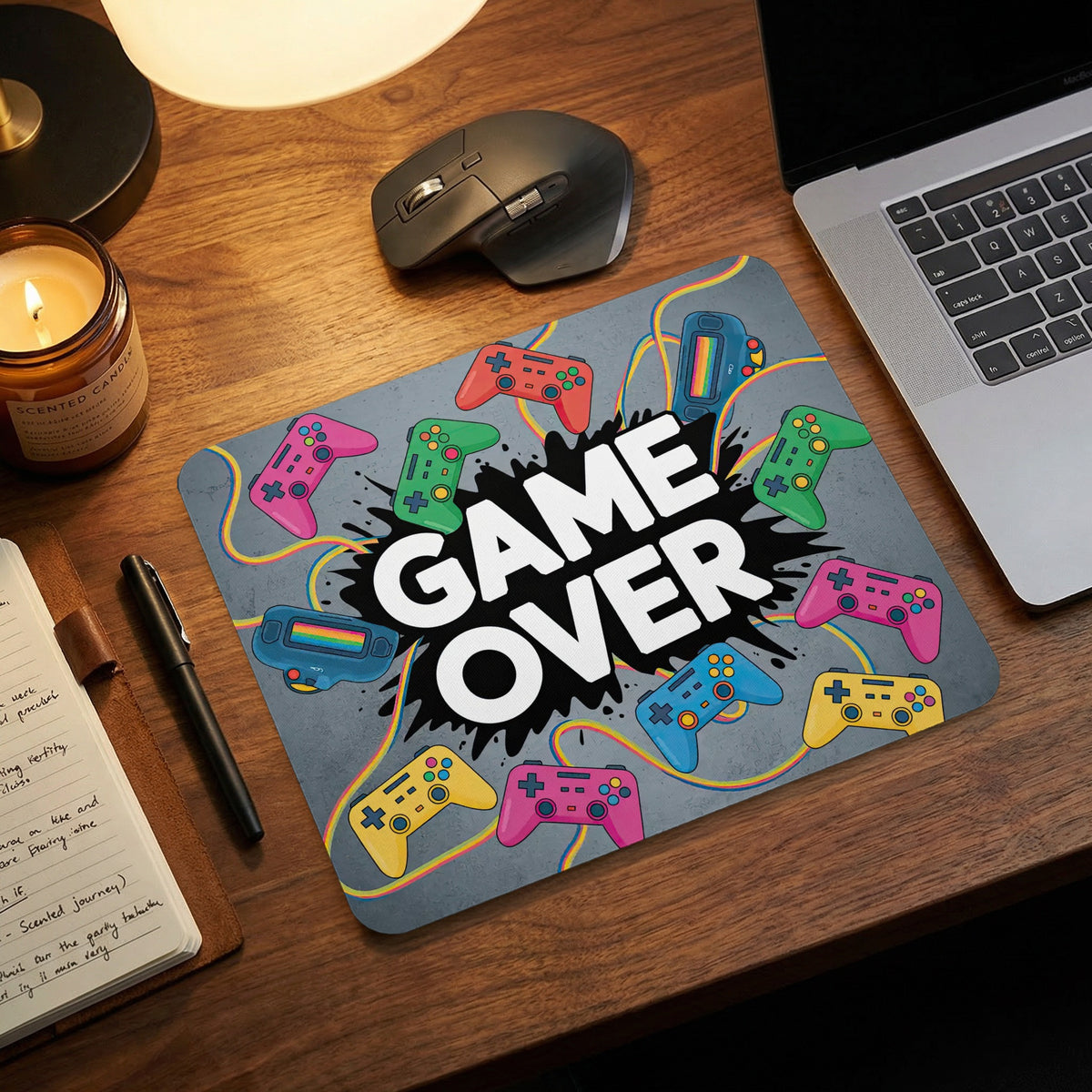 A gray mouse pad with colorful game controllers and bold white Game Over text sits on a wooden desk.